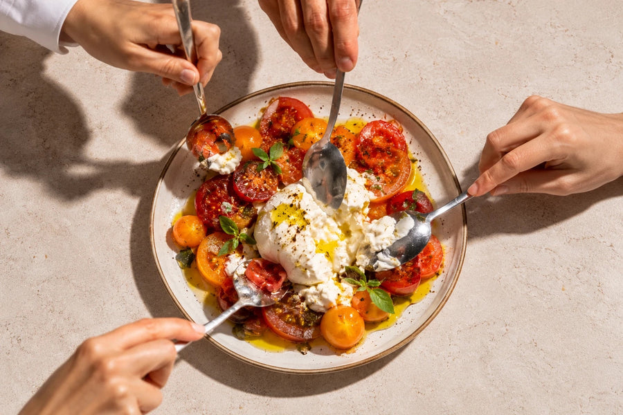 Burrata mit Tomaten und Olivenöl, vier Hände greifen mit Löffeln zu